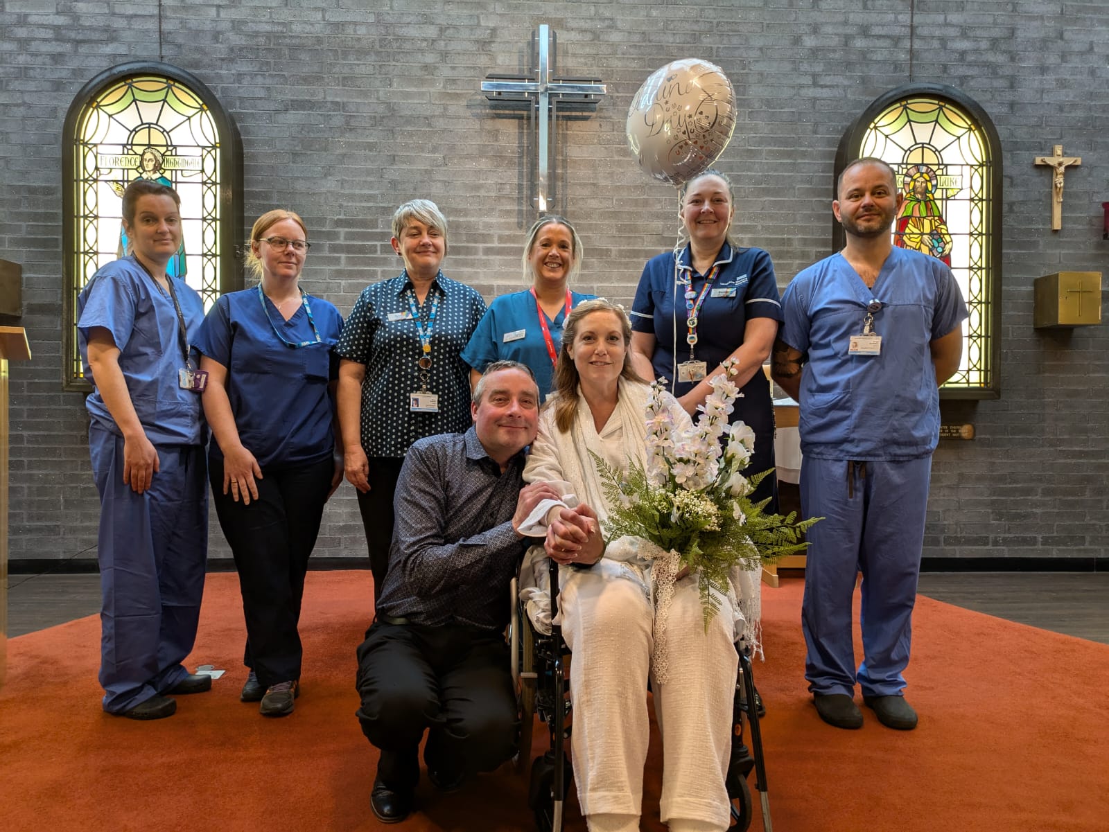 Photo of the married couple in the chaplaincy setting with several medical staff in uniform behind them, smiling