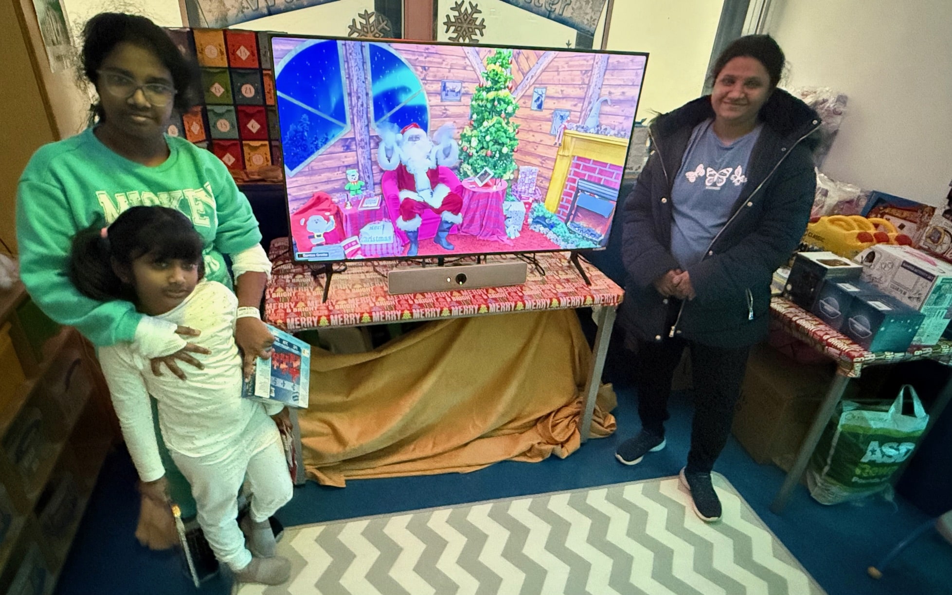 People standing next to a TV, depicting Santa, smiling, while having received a gift