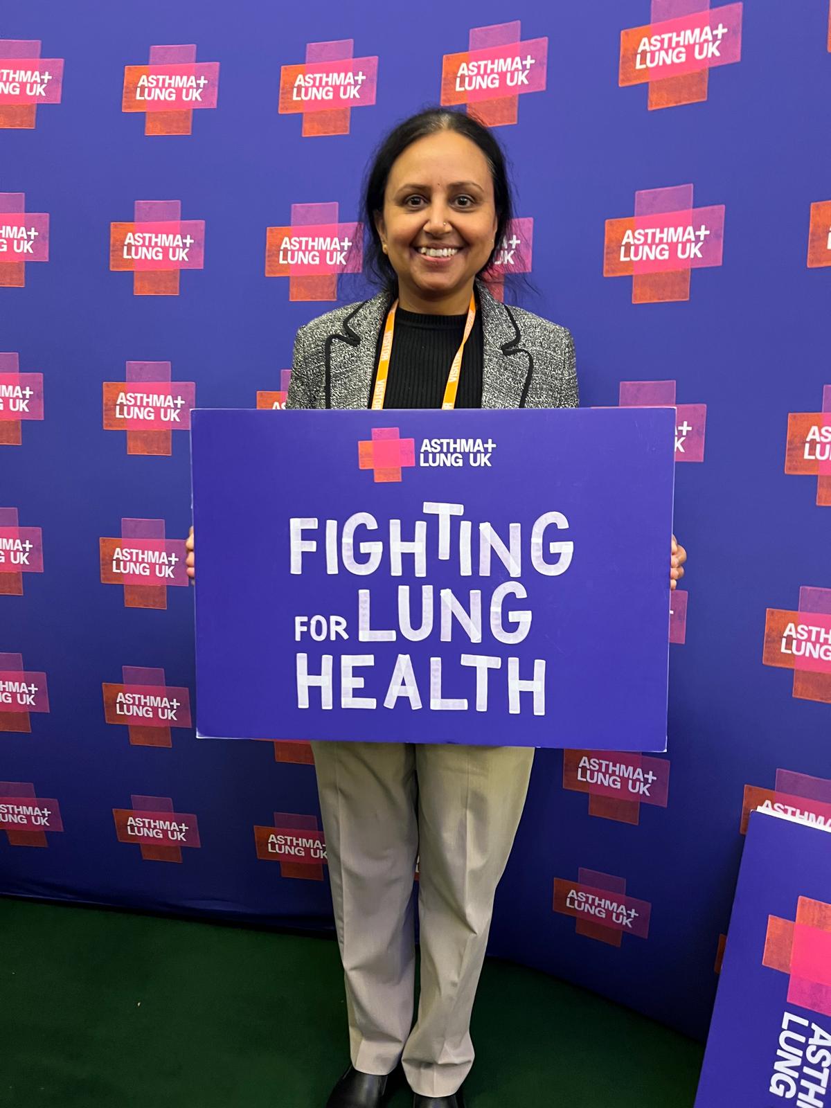 A photo of Dr Gudur holding an Asthma+ Lung UK placard, smiling