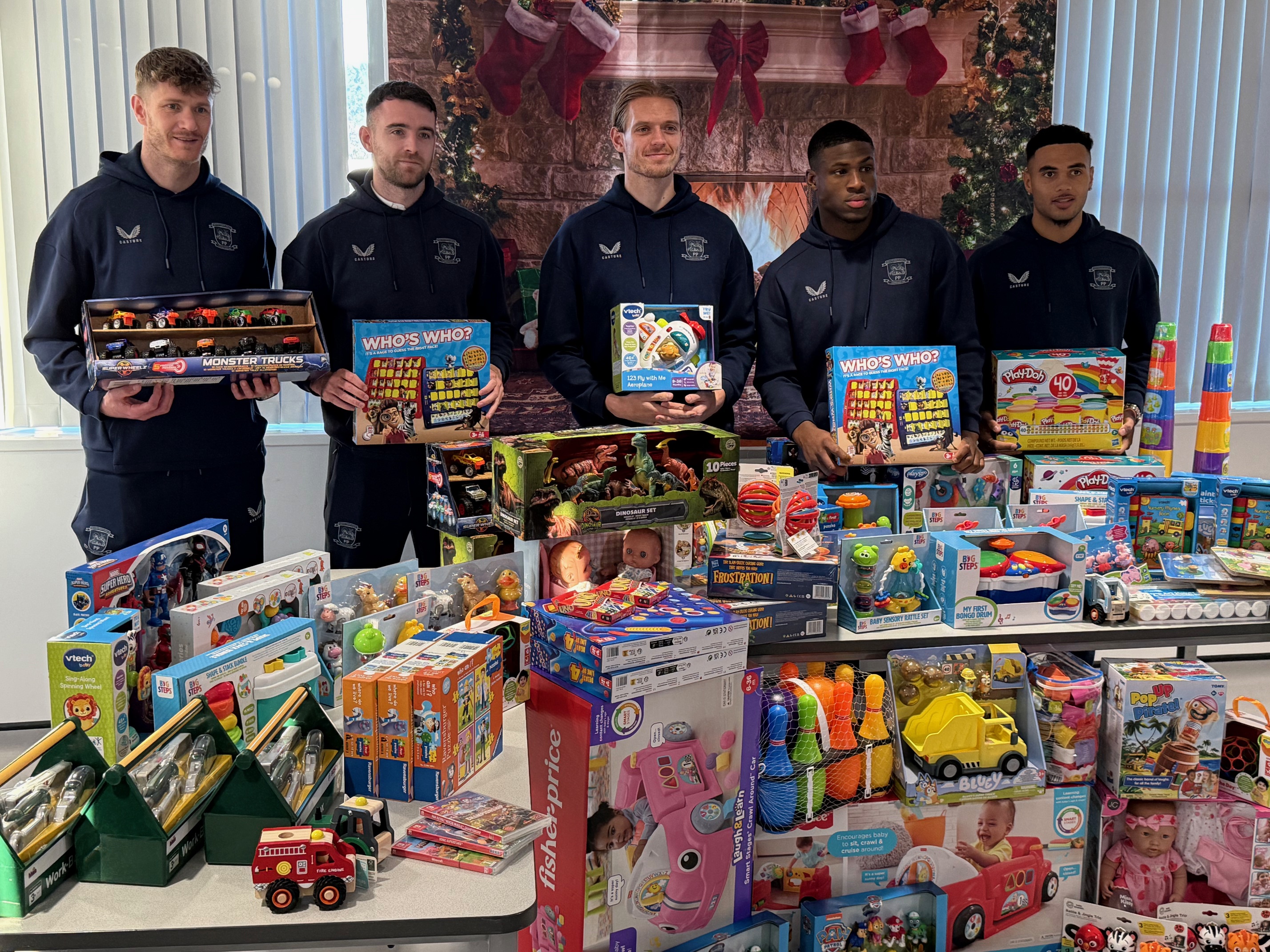 PNE football players holding Christmas while standing behind a very big collection of more Christmas gifts