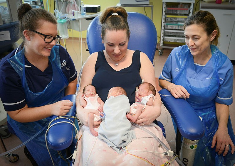 A photo depicting two female NHS staff members, a mother and her triplet babies